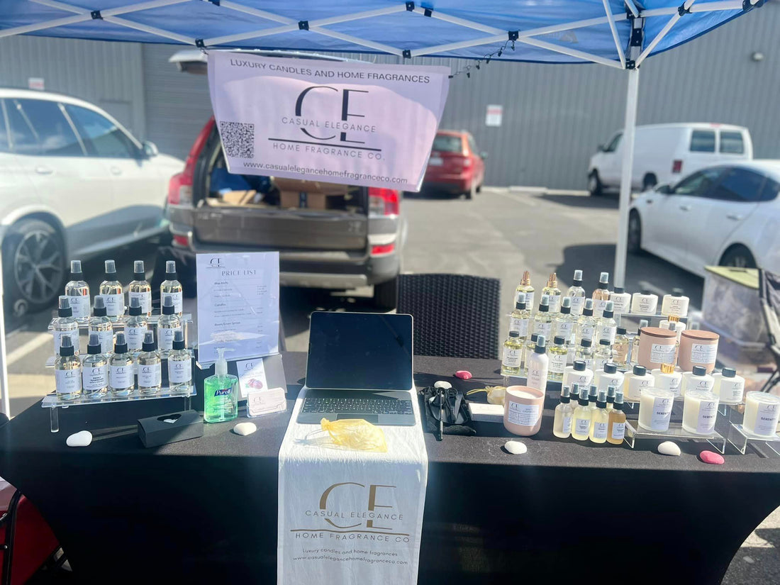 Table outdoors at a vendor event with black tablecloth.  Room Sprays and candles are sitting on the table.